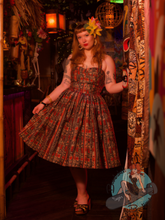 Redhead pinup girl at tiki bar wearing Alfred Shaheen inspired 1950s vintage style swing dress with halter straps.