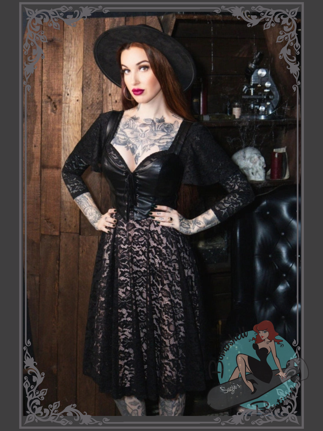 Woman in a black dress with lace details and a wide-brimmed hat standing in a rustic setting.