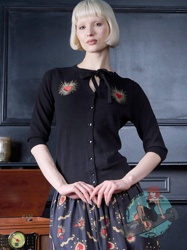 Pinup girl wearing black button-front cardigan with embroidered red hearts and gold rays on the chest by banned retro canada.
