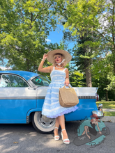 Pinup girl wearing swing dress with wide brim vintage straw hat in front of classic car