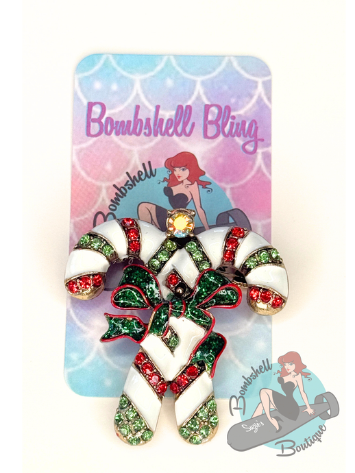 Candy cane-shaped brooch with gemstones on a 'Bombshell Bling' branded card.