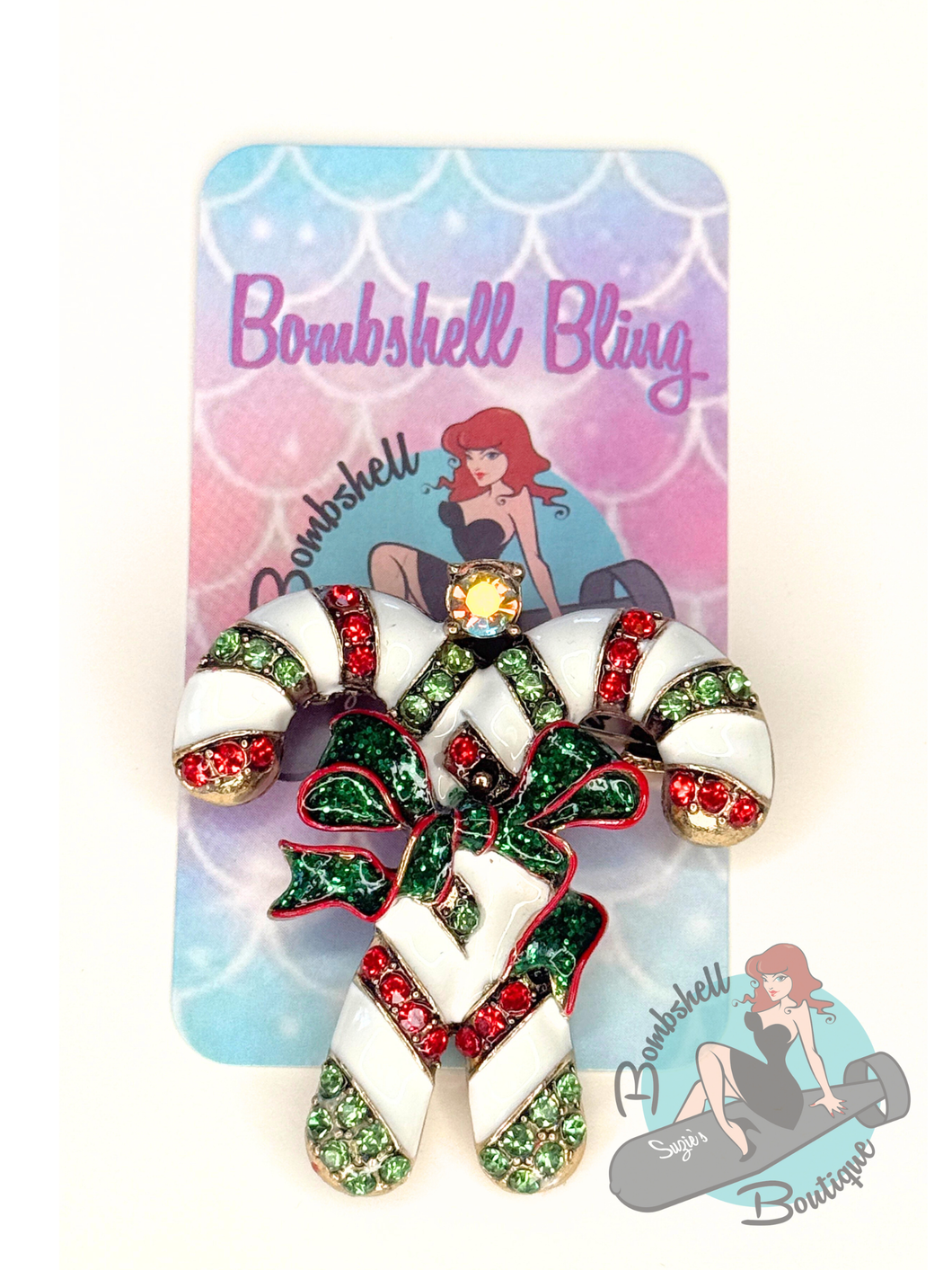 Candy cane-shaped brooch with gemstones on a 'Bombshell Bling' branded card.