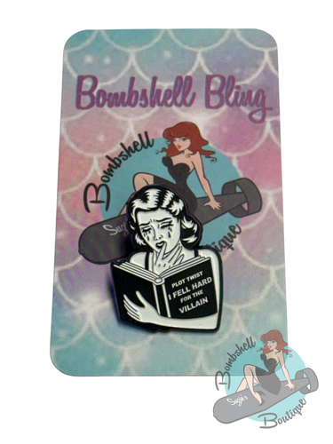 Pin with illustration of a woman reading a book titled 'I Fell Hard for a Villain' on a 'Bombshell Bling' card.