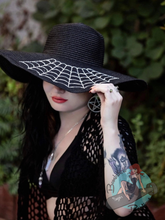 Goth pinup wearing large brim floppy sunhat with spiderweb embroidery on it