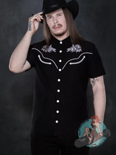 Rockabilly man wearing a Katakomb black short-sleeve western-style button-up shirt with white embroidered details and a black cowboy hat.