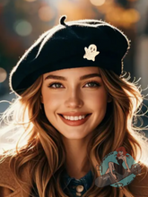 Woman wearing a black beret with a ghost design, smiling outdoors.