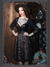 Woman in a black dress with lace details and a wide-brimmed hat standing in a rustic setting.